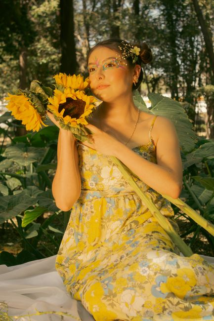 Fotomural Mujer con pintura facial vibrante sosteniendo girasoles en un frondoso bosque.