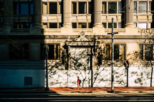 A solitary runner in red jogs through shadows cast by an urban building in Portland.
