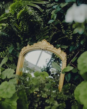 Elegant gold-framed mirror amidst lush, vibrant greenery reflecting the beauty of nature.