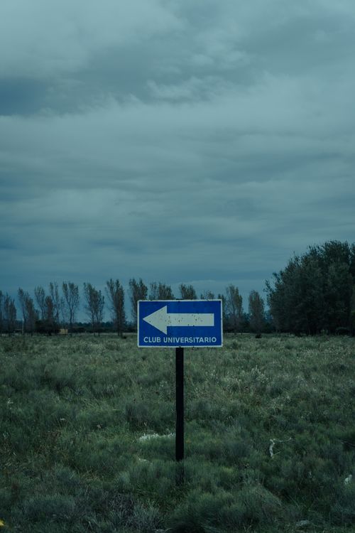 Free A directional sign points through a field under a cloudy sky in Rosario, Argentina. Stock Photo