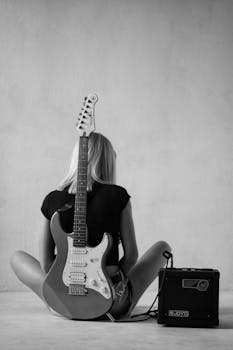 Artistic black and white photo of a woman sitting with an electric guitar and amplifier.