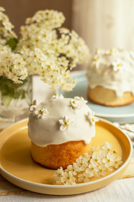 Decorative Easter cake with white icing and flowers, surrounded by spring blossoms.