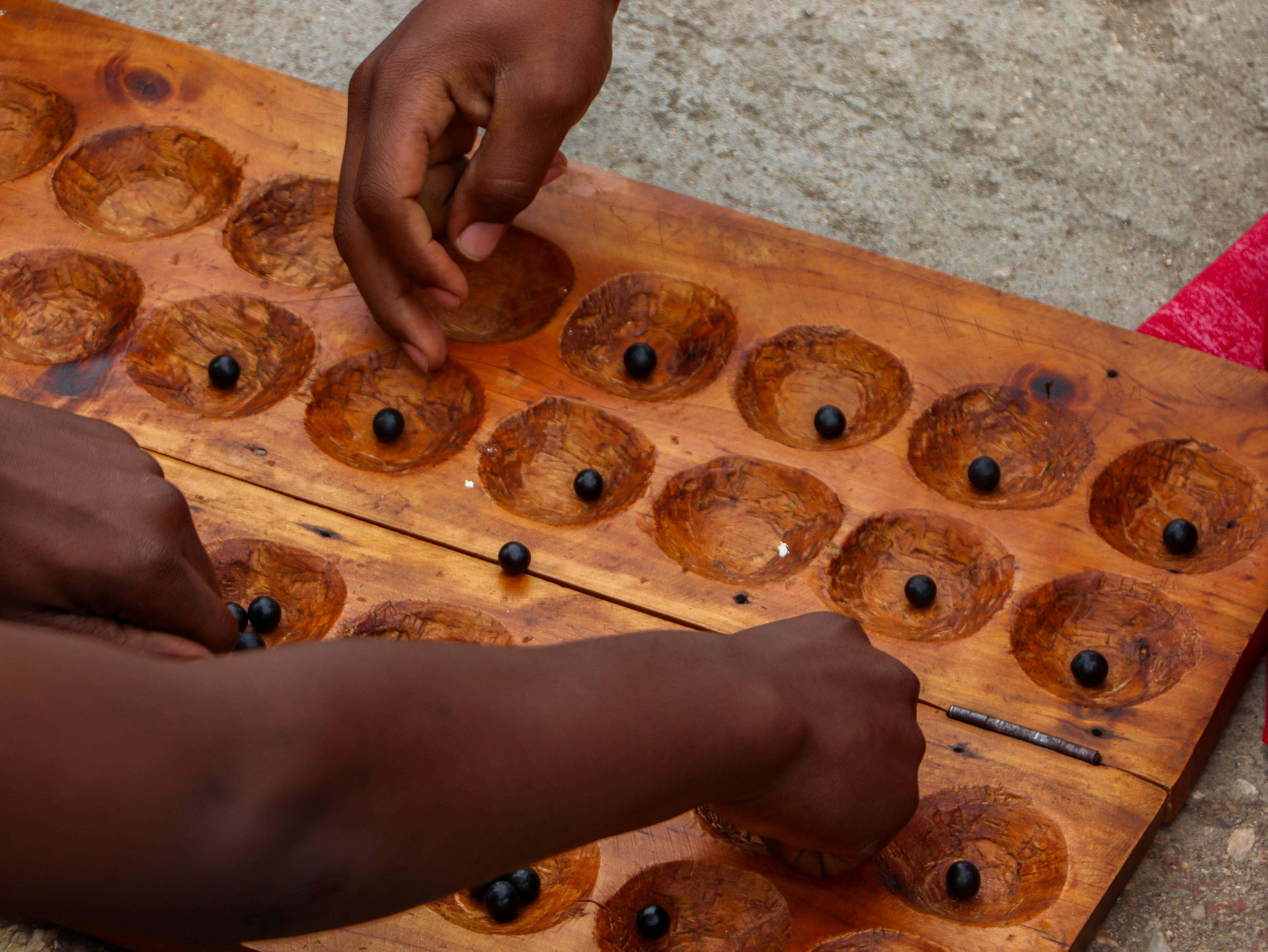 Hands engaging in the traditional Rwandan game Urusoro, played on a wooden board outdoors.