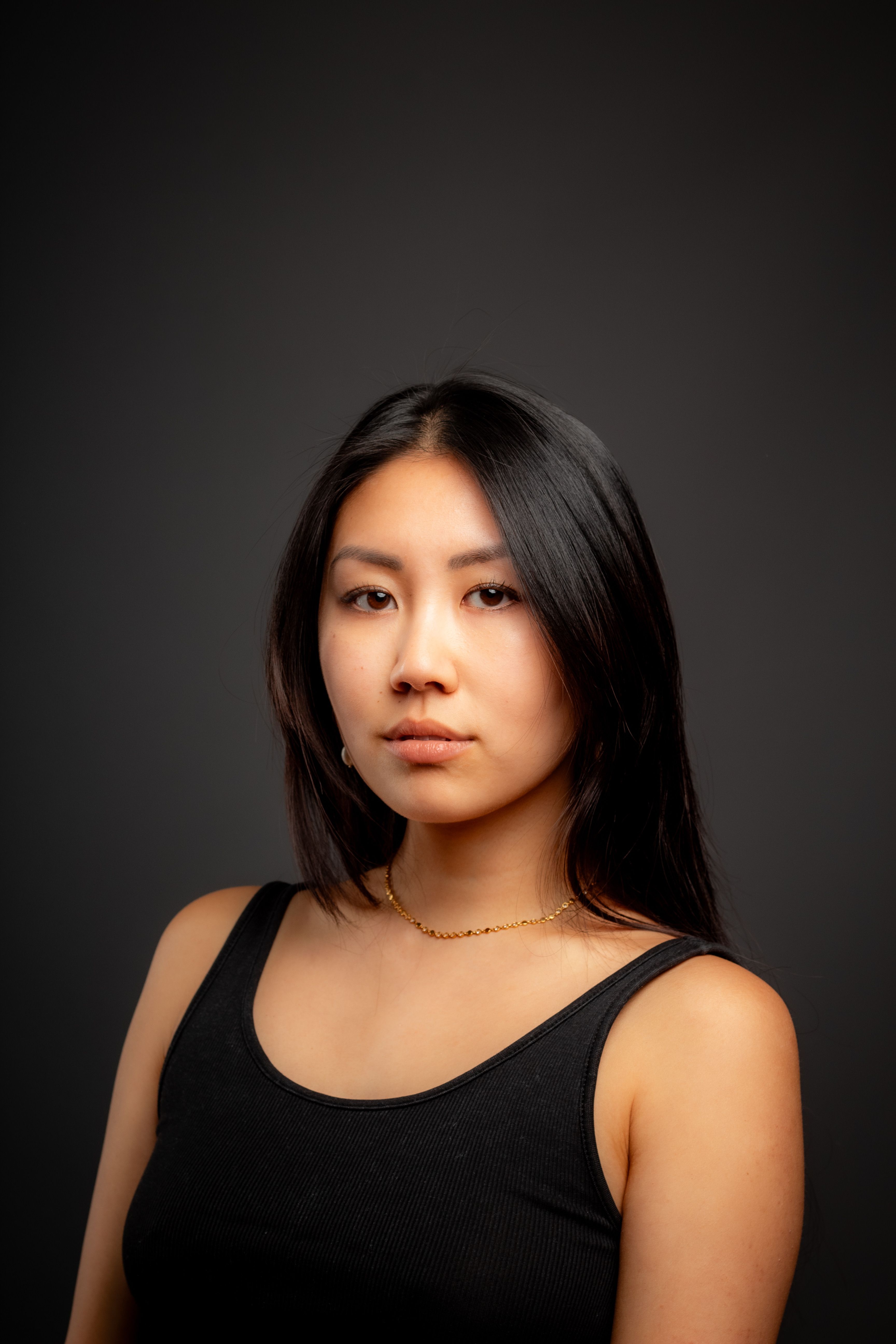 Studio portrait of a young woman with long hair and a neutral expression, soft lighting.