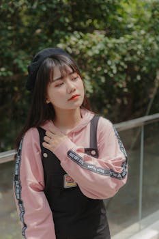 一位身穿粉红色连帽衫和黑色工作服的年轻女子正在户外与绿色植物合影