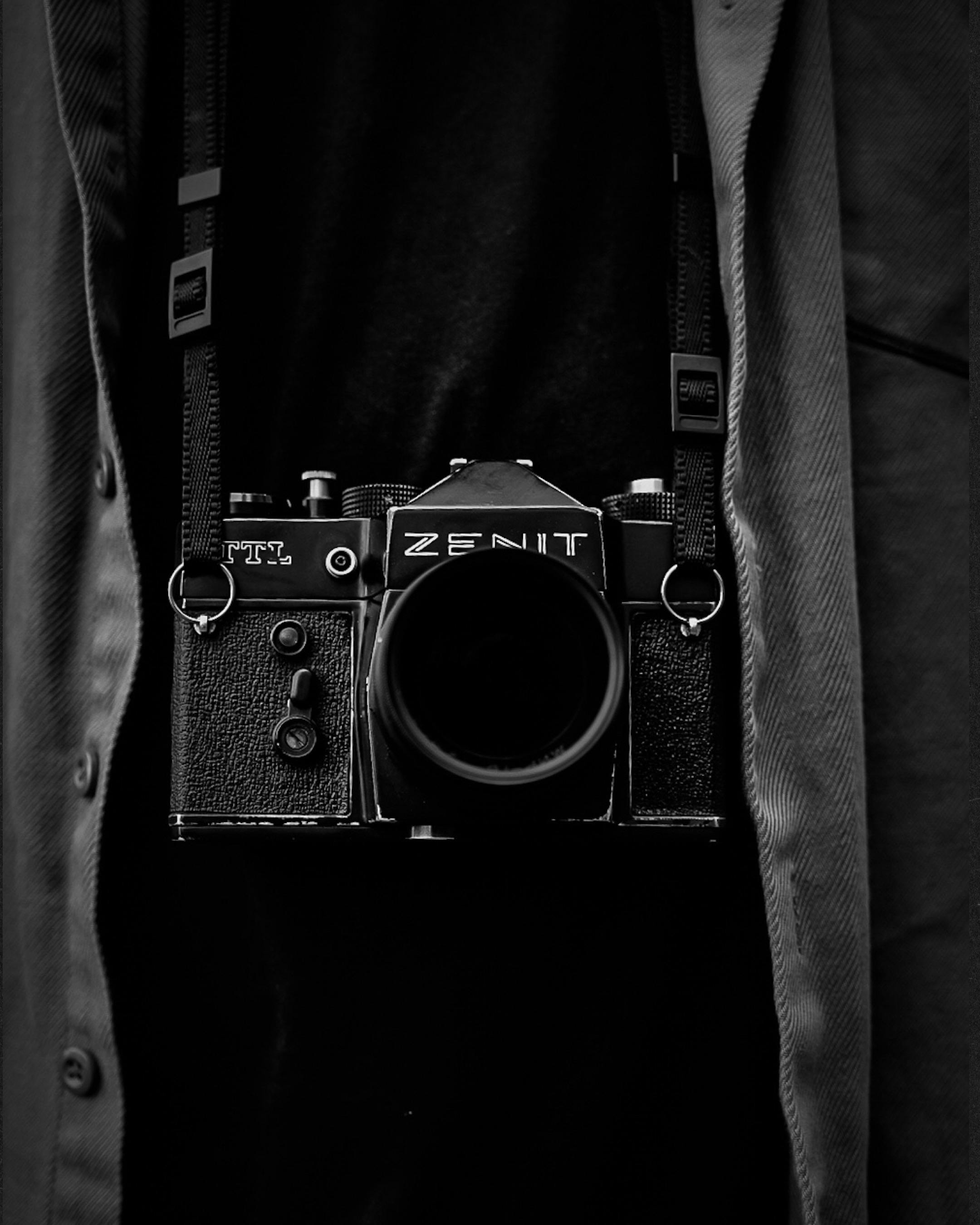 Monochrome photo of a vintage Zenit camera hanging around a neck, evoking nostalgia.