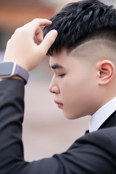 Close-up profile of a young man adjusting hair, wearing a suit and smartwatch.