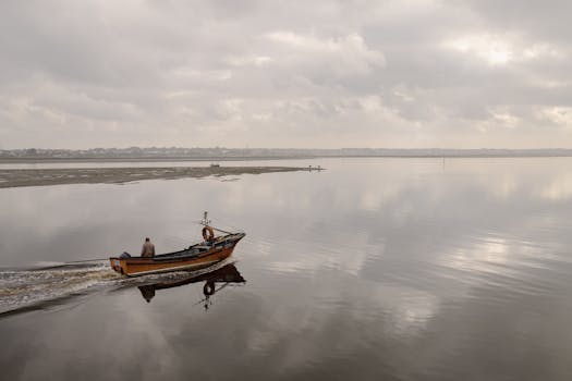 A lone boat sails quietly across the calm waters of Ria de Aveiro, Portugal under a cloudy sky.