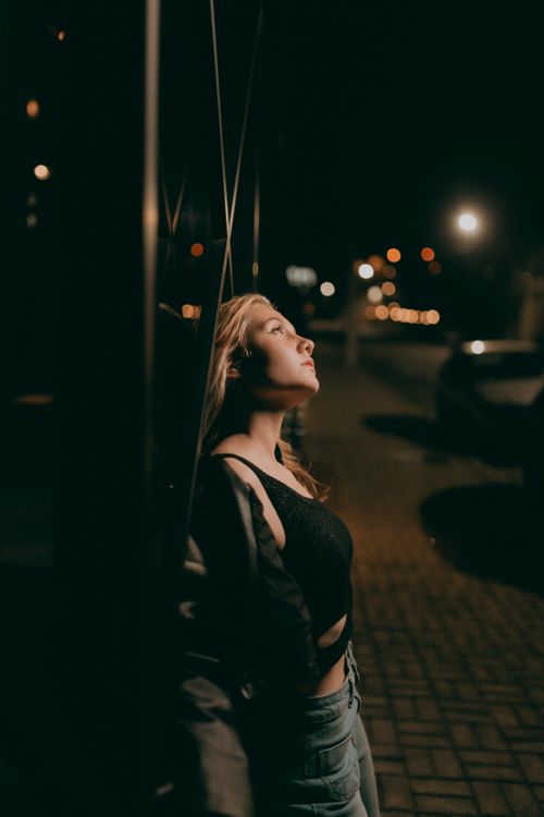 Free A woman stands against a wall under glowing streetlights, contemplating in the quiet of the night. Stock Photo
