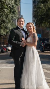 A happy couple posing in wedding attire on a sunny street in Houston, Texas.