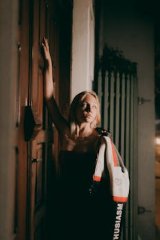 A fashionable woman posing outdoors at night against a wooden door.