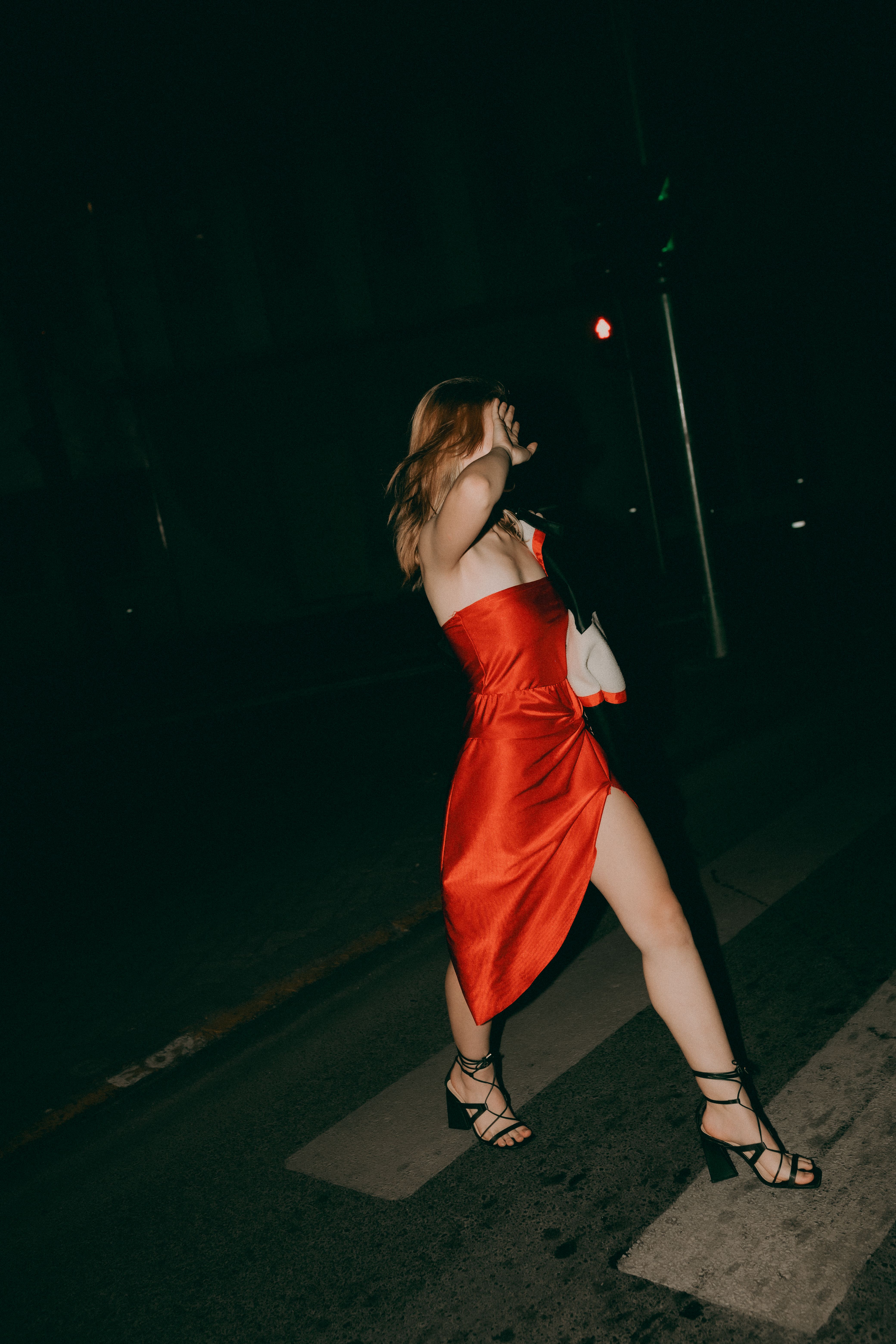 Stylish woman in a red dress crossing a street at night, exuding fashion and elegance.