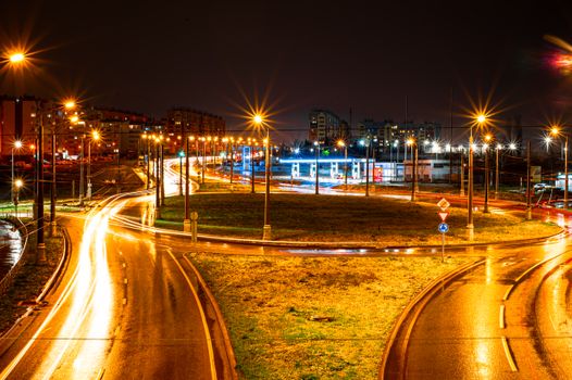 Long exposure of a city roundabout at night showcasing vibrant light trails and streetlights.