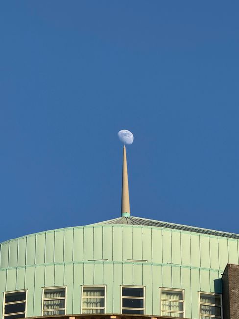 A striking view of the moon aligned with a spire atop a building in The Hague.