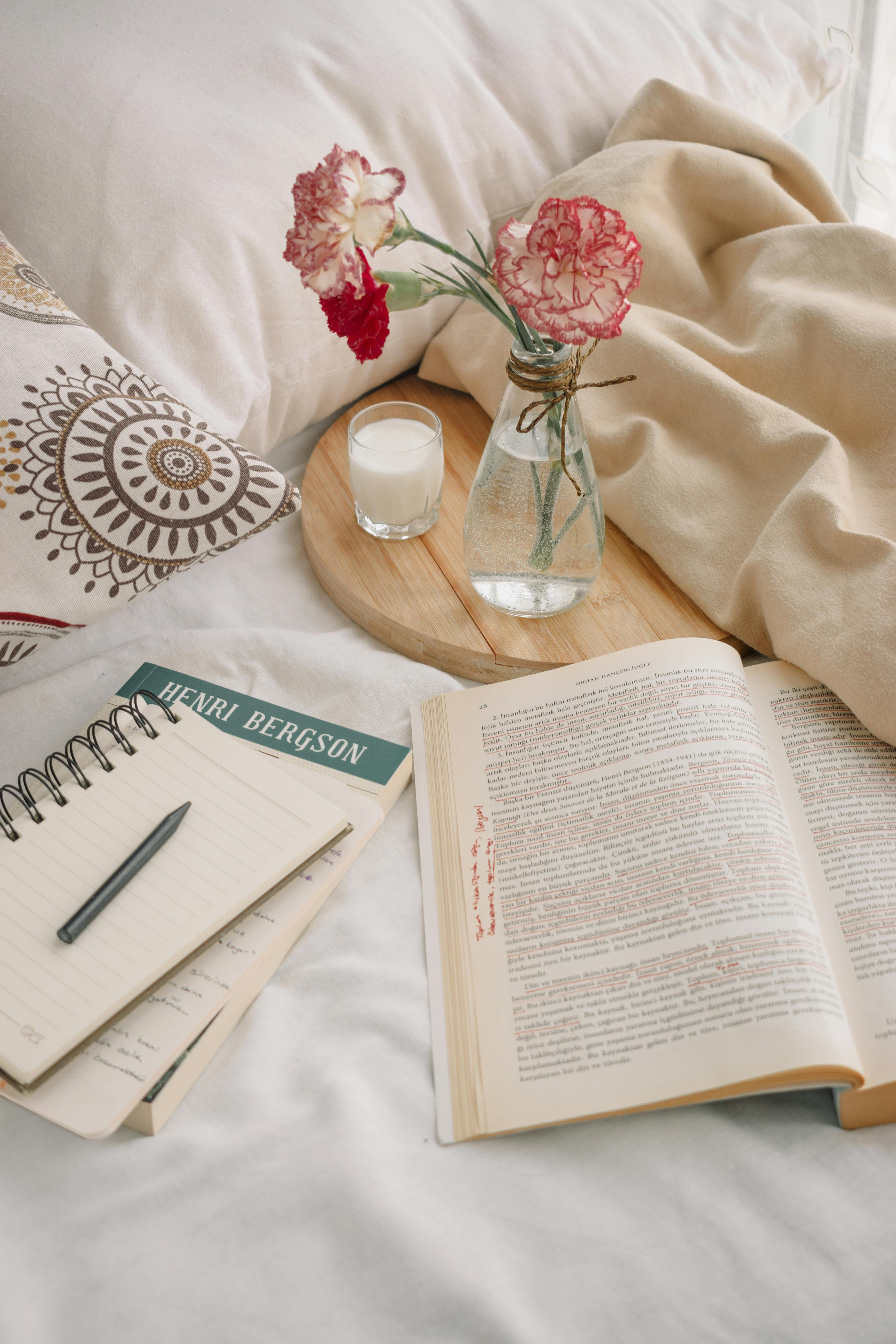 A peaceful morning setup with books, flowers, and a drink on a cozy bed.
