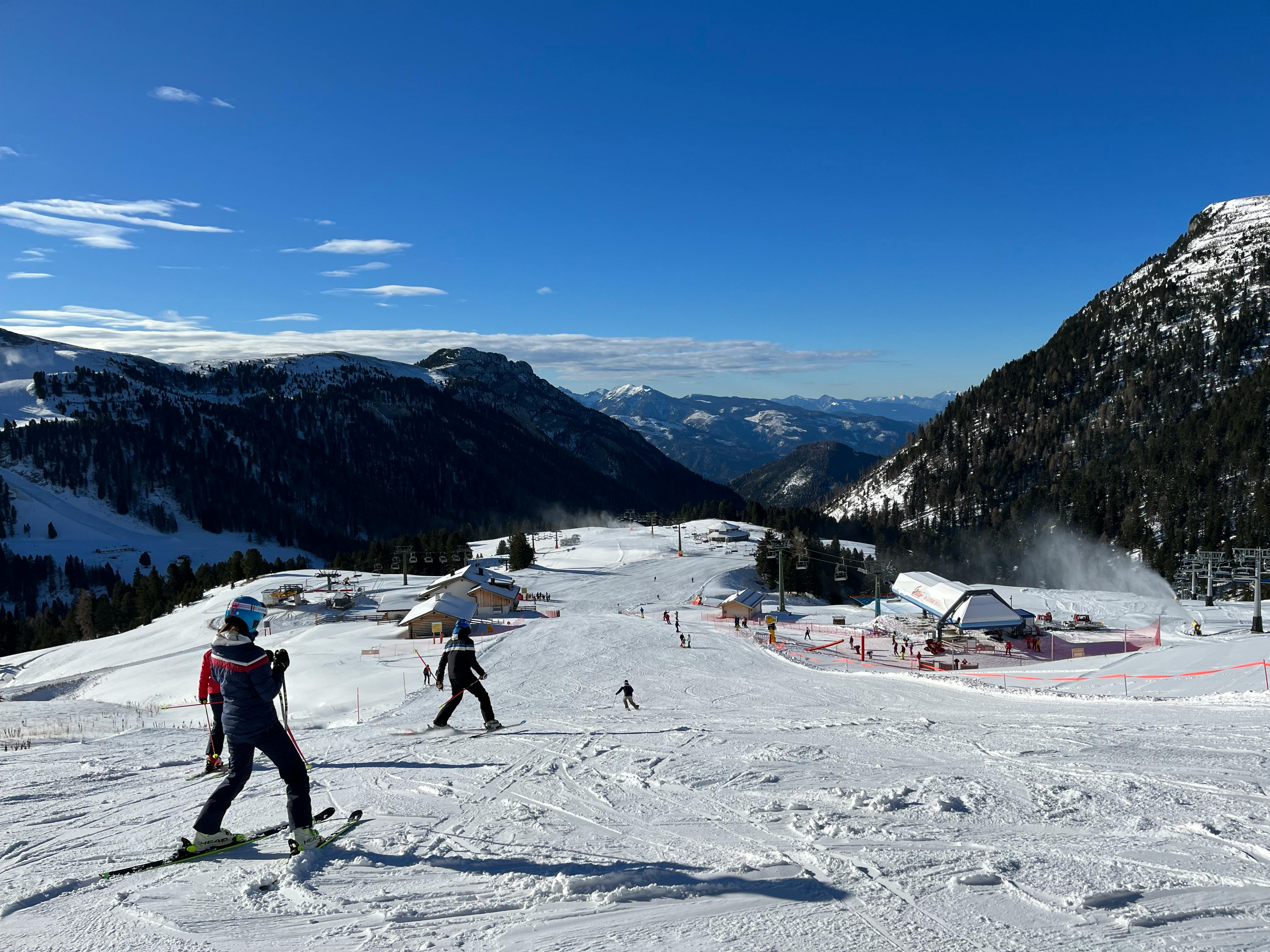 Skiers enjoy the snowy slopes of Pampeago in Trentino-Alto Adige, Italy, under a clear blue sky.