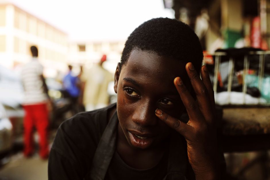 Thoughtful young boy sitting outdoors in a busy street scene in Abuja, Nigeria.
