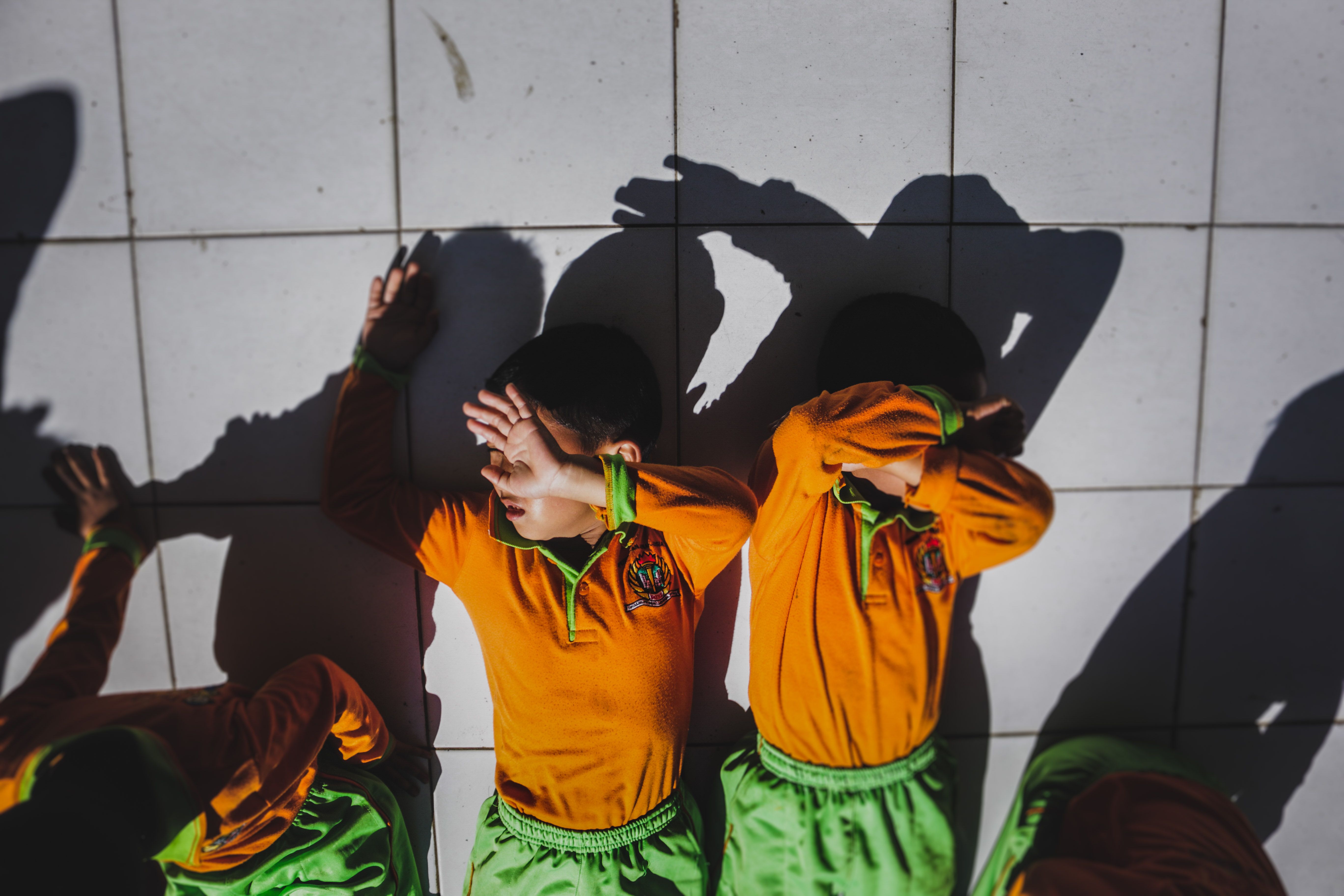 Group of children in school uniforms blocking sunlight on tiled floor.