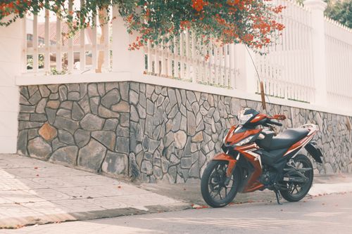 Free Stylish red motorcycle parked by a stone wall with flowers. Stock Photo