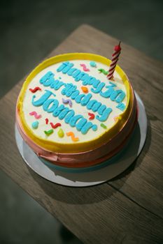 A vibrant birthday cake with blue frosting, confetti, and a single red candle on a wooden table.