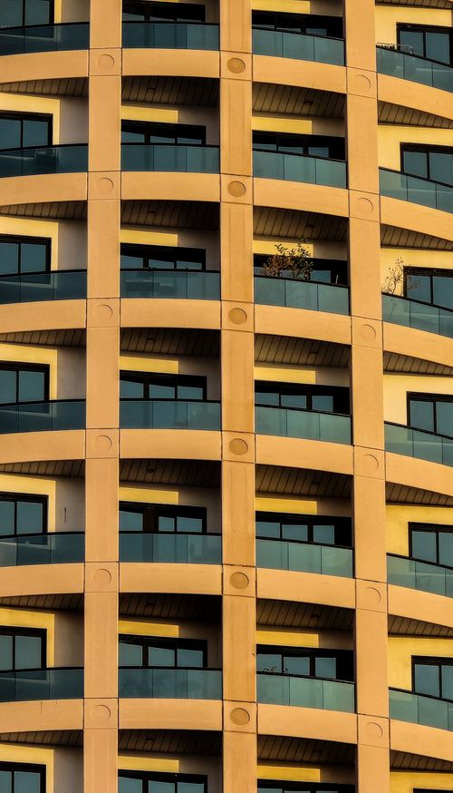 Free High-rise building facade in Dubai, showcasing modern architecture with curved balconies and warm lighting. Stock Photo