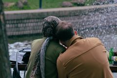 Older couple sitting by a fountain, sharing a peaceful moment in a city park.