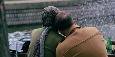 Older couple sitting by a fountain, sharing a peaceful moment in a city park.