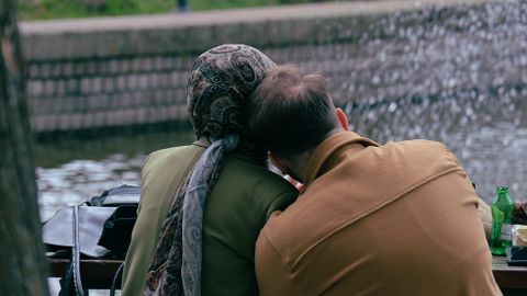 Older couple sitting by a fountain, sharing a peaceful moment in a city park.