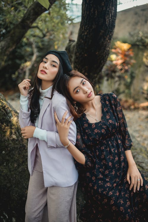 Two Women leaning on each other standing under a tree