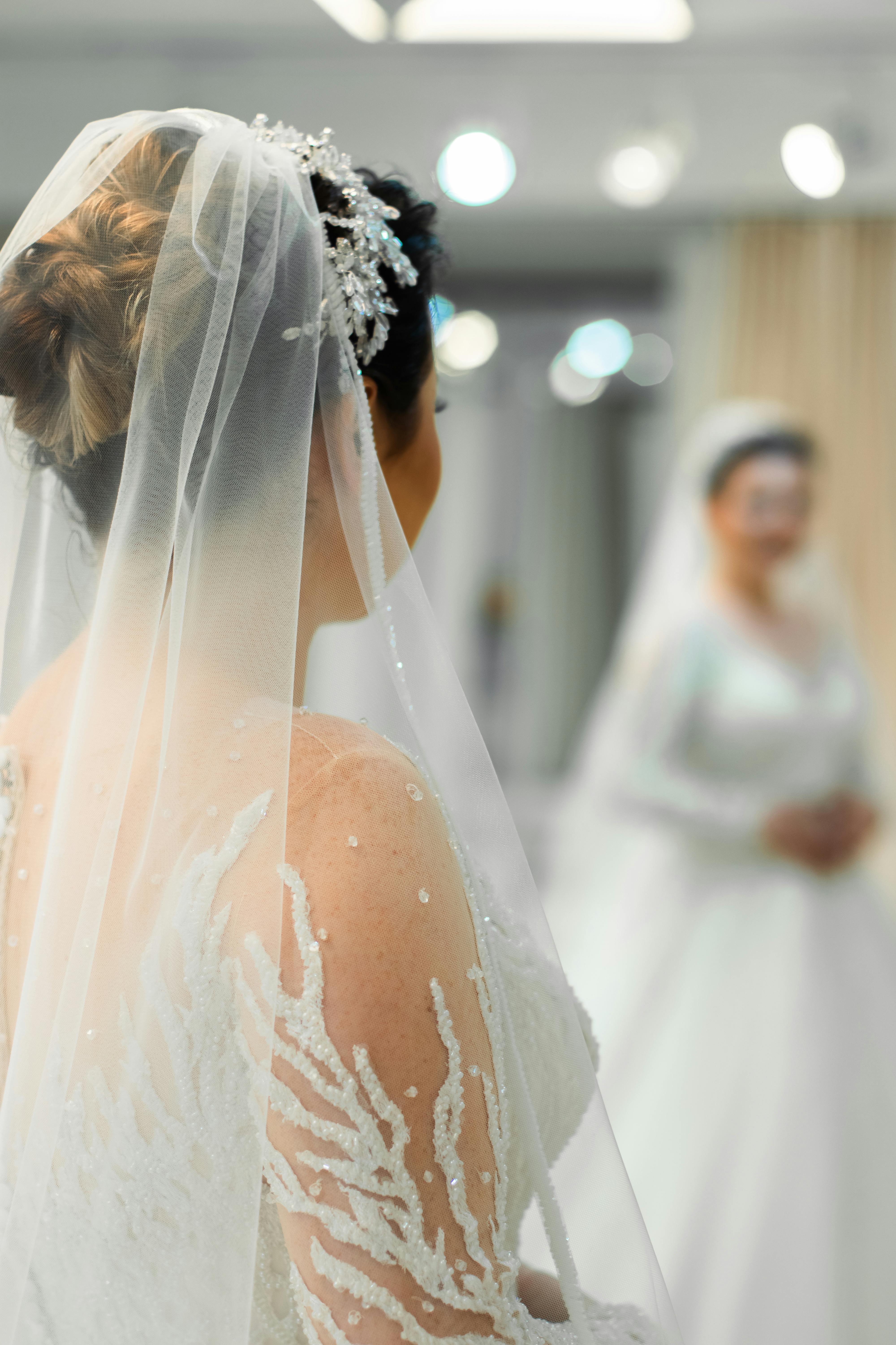 A bride in Turkey elegantly adjusts her veil while viewing her reflection in a mirror, captured in a bridal boutique.