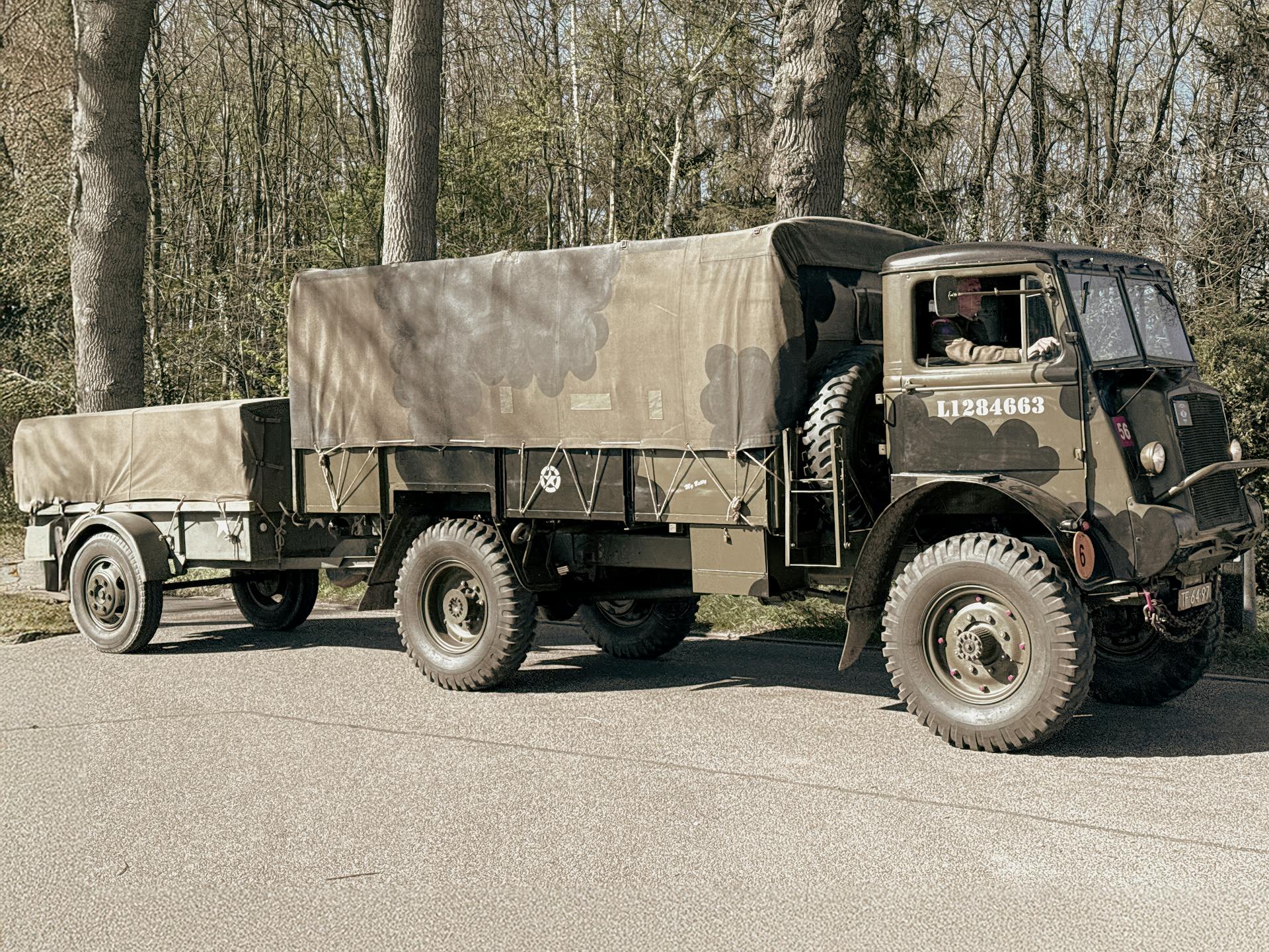 Classic military truck with trailer parked on a forest road during the day.