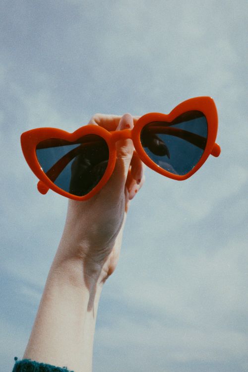 Free Bright red heart sunglasses against a clear blue sky. Perfect for summer vibes. Stock Photo