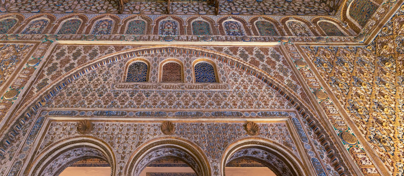 Explore the ornamental arches and ceilings of Seville's Real Alcázar, showcasing stunning Mudéjar architecture.