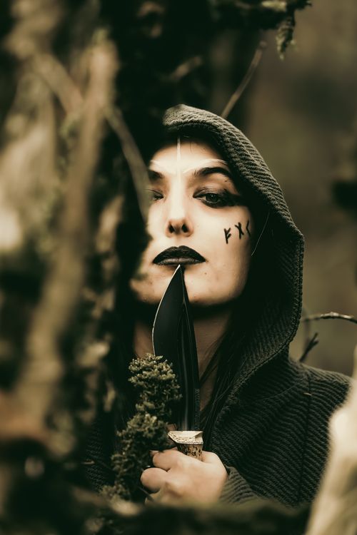 Free A mysterious person in a forest holding a knife with facial markings, creating a moody atmosphere. Stock Photo