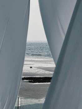A peaceful beach scene captured through soft, flowing curtains, creating a sense of tranquility and escape.