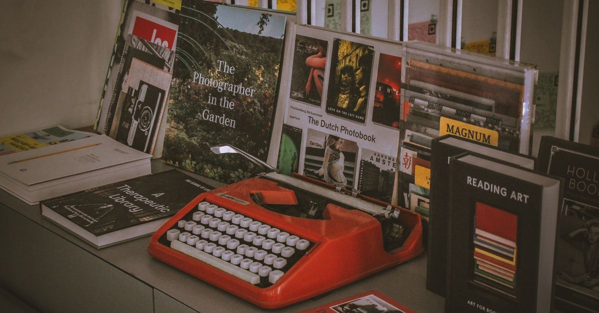 A vibrant red vintage typewriter surrounded by a collection of photobooks and literature in an artistic setup.