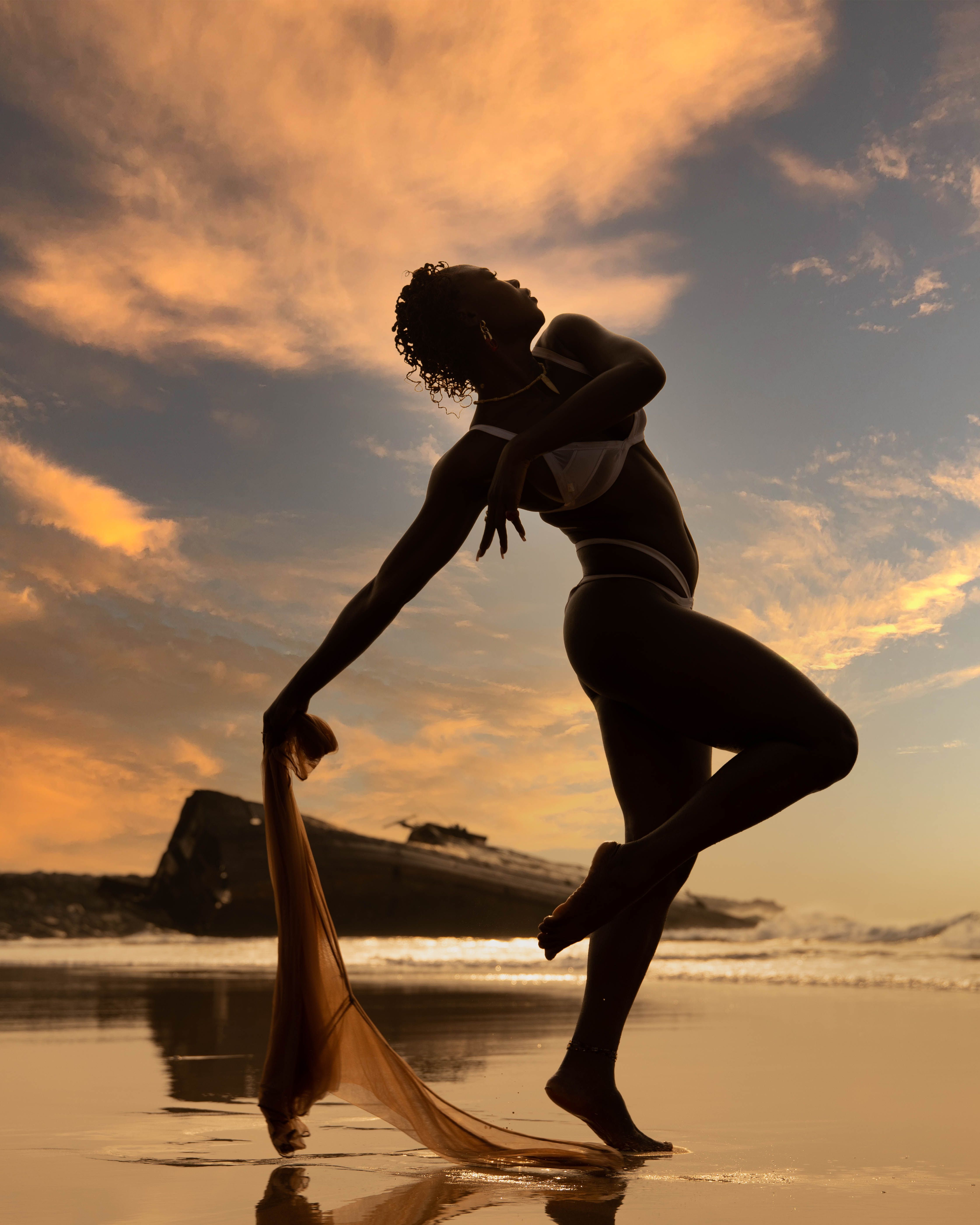 Elegant silhouette of a dancer posing gracefully on a beach during sunset with vibrant skies.