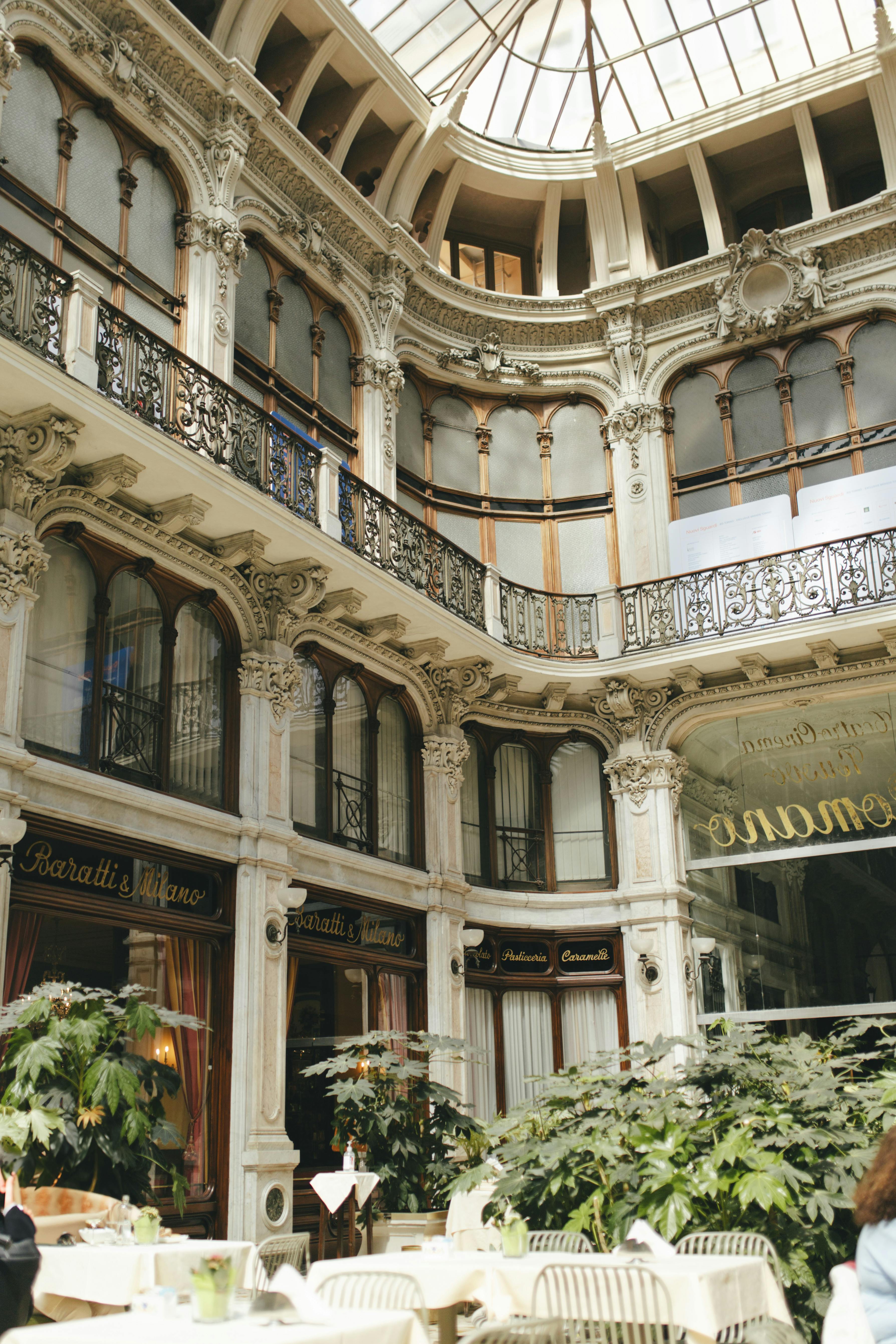 Beautiful indoor café within a historic European arcade featuring ornate architecture and lush plants.