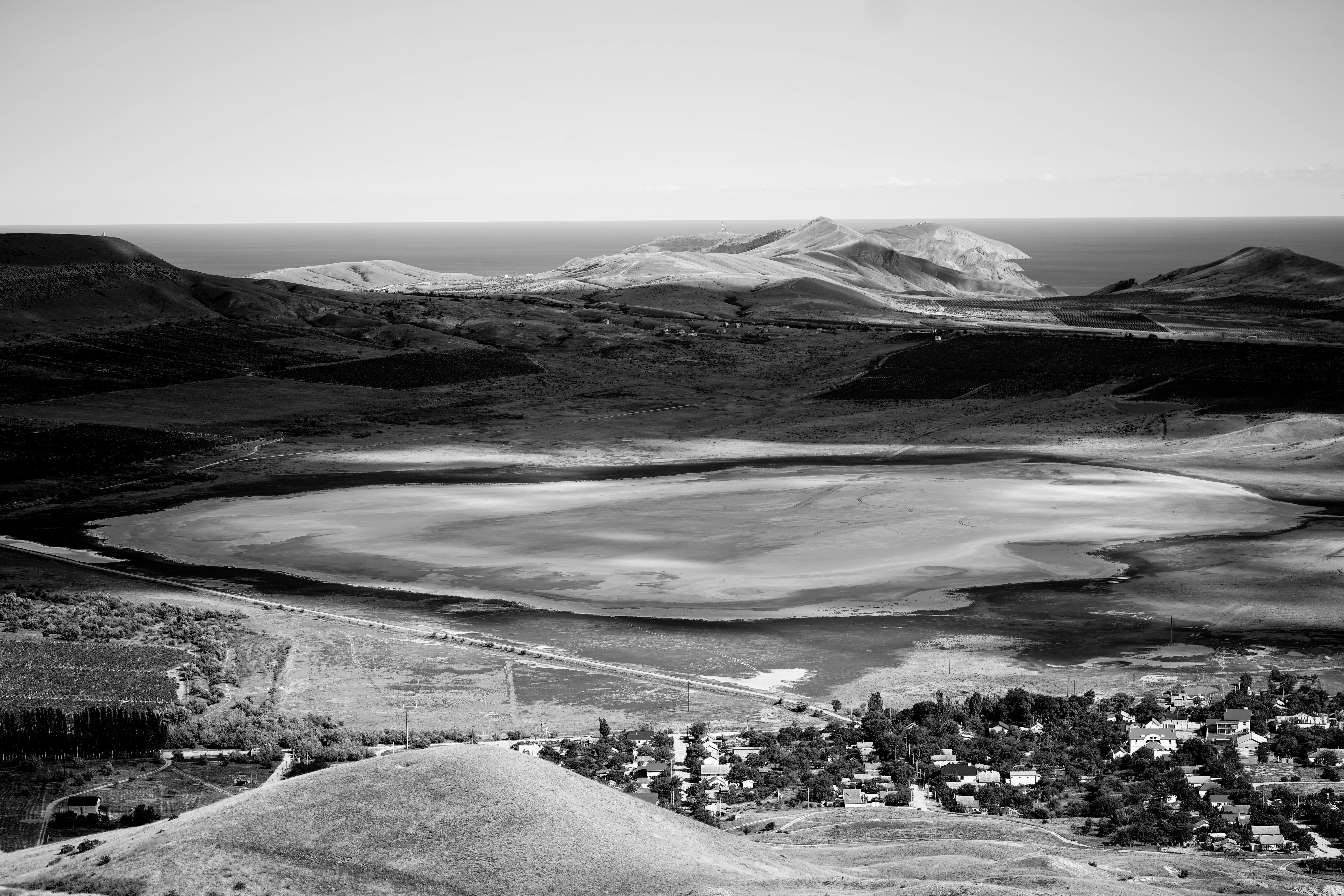 Scenic aerial view of Koktebel's unique landscape featuring hills, coastline, and a dry lake in monochrome.