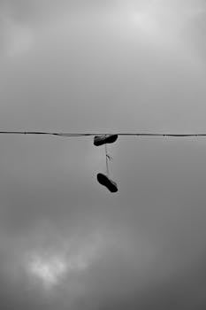 A pair of shoes hanging from a wire against a cloudy, dramatic sky in Oslo.
