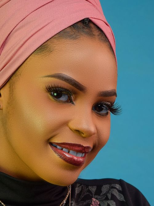 Free Close-up portrait of a smiling woman in a pink headwrap against a blue background. Stock Photo