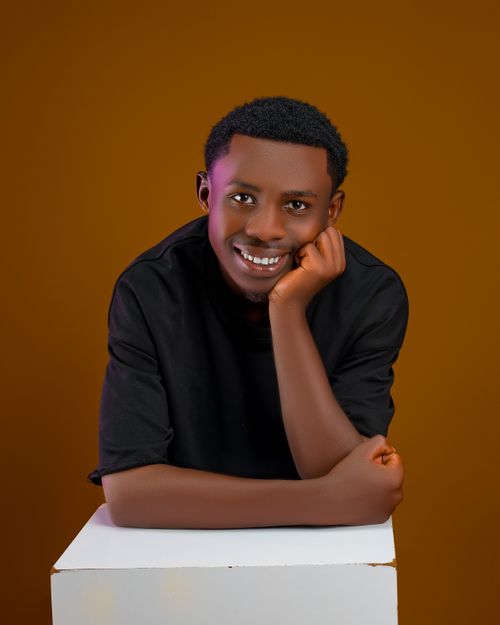 Free Portrait of a smiling young man leaning forward on a surface, against a warm brown backdrop. Stock Photo