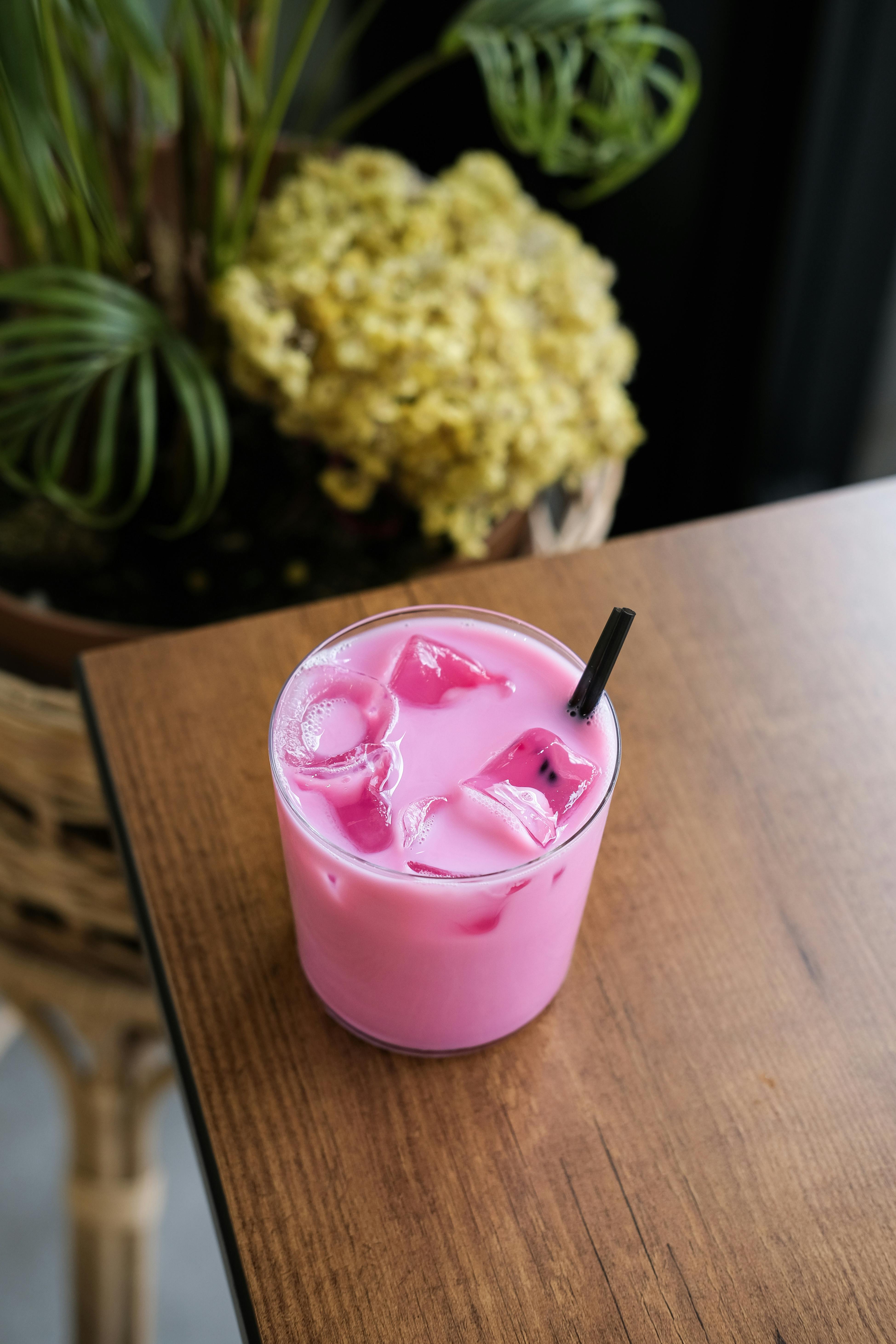 Refreshing pink iced beverage with straw on a wooden table in a cozy setting.