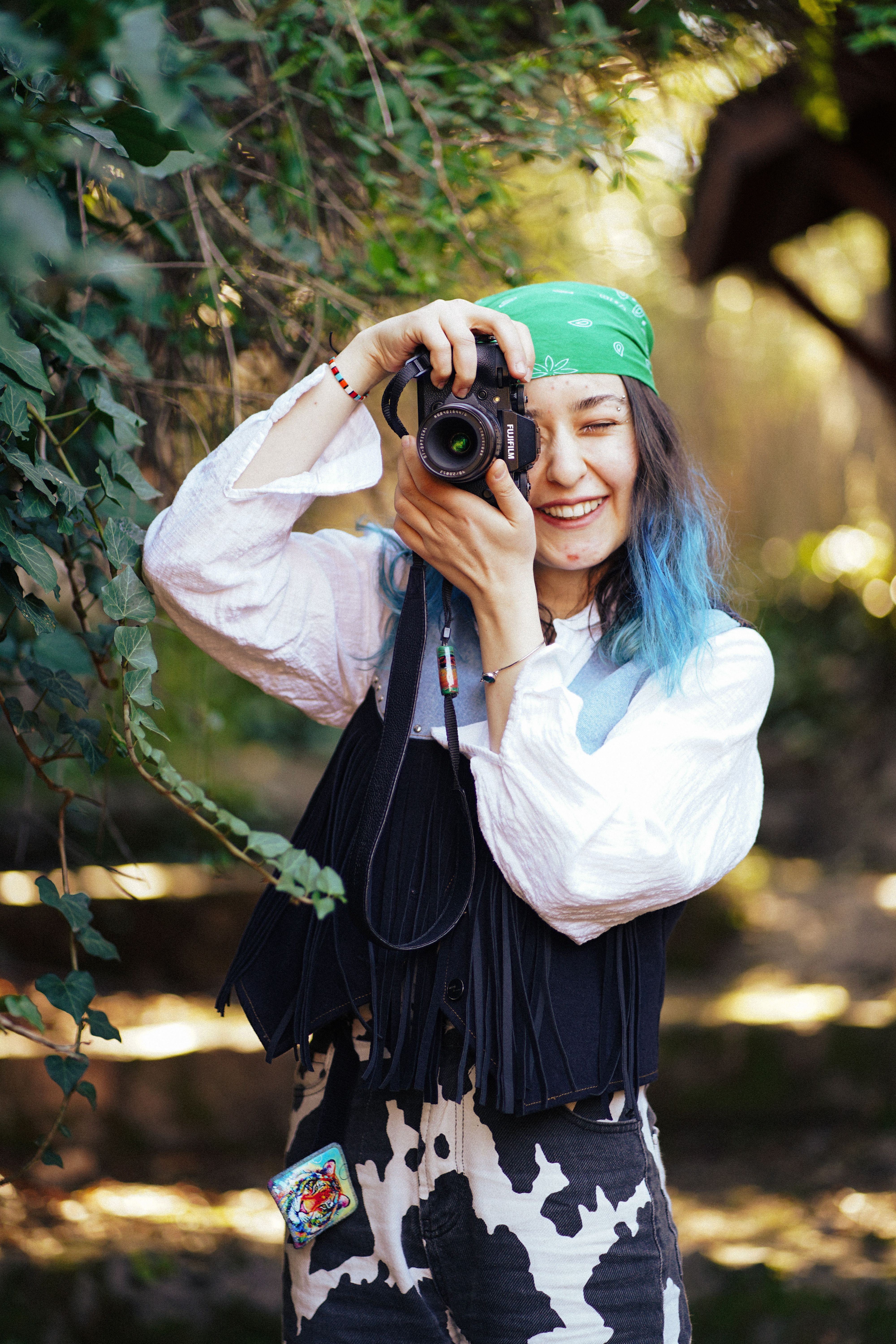 A cheerful female photographer with blue hair capturing nature outdoors.