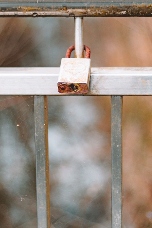 Free Close-up of a rusty padlock on a weathered metal fence, symbolizing security and decay. Stock Photo