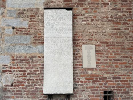 Historic stone inscription on a rustic brick wall in Milan.