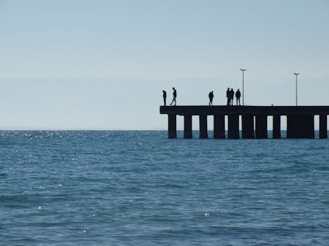 Silhouettes of people standing on a pier with a beautiful Mediterranean backdrop in Calabria, Italy.
