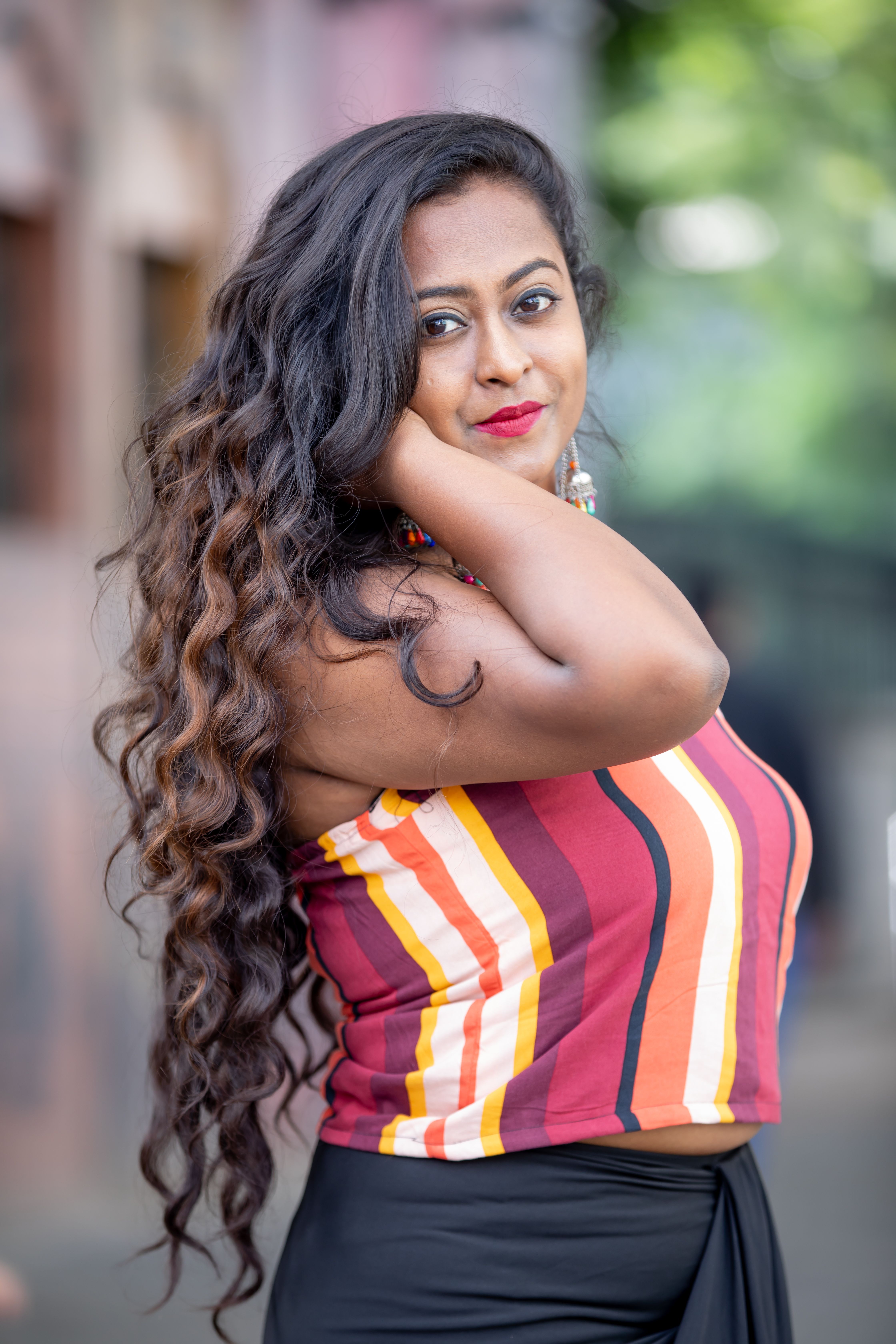 Stylish Indian woman with long curly hair posing in a vibrant top outdoors.