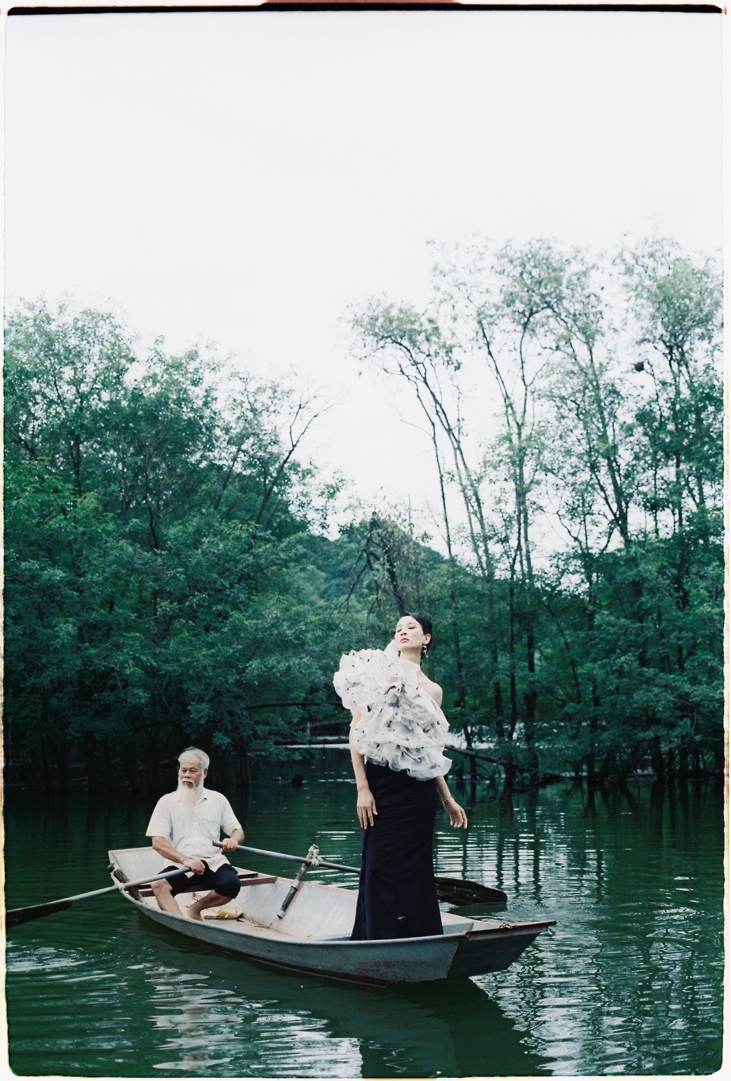 A stylish photoshoot featuring an elegant woman and an elderly man in a boat on a peaceful lake.