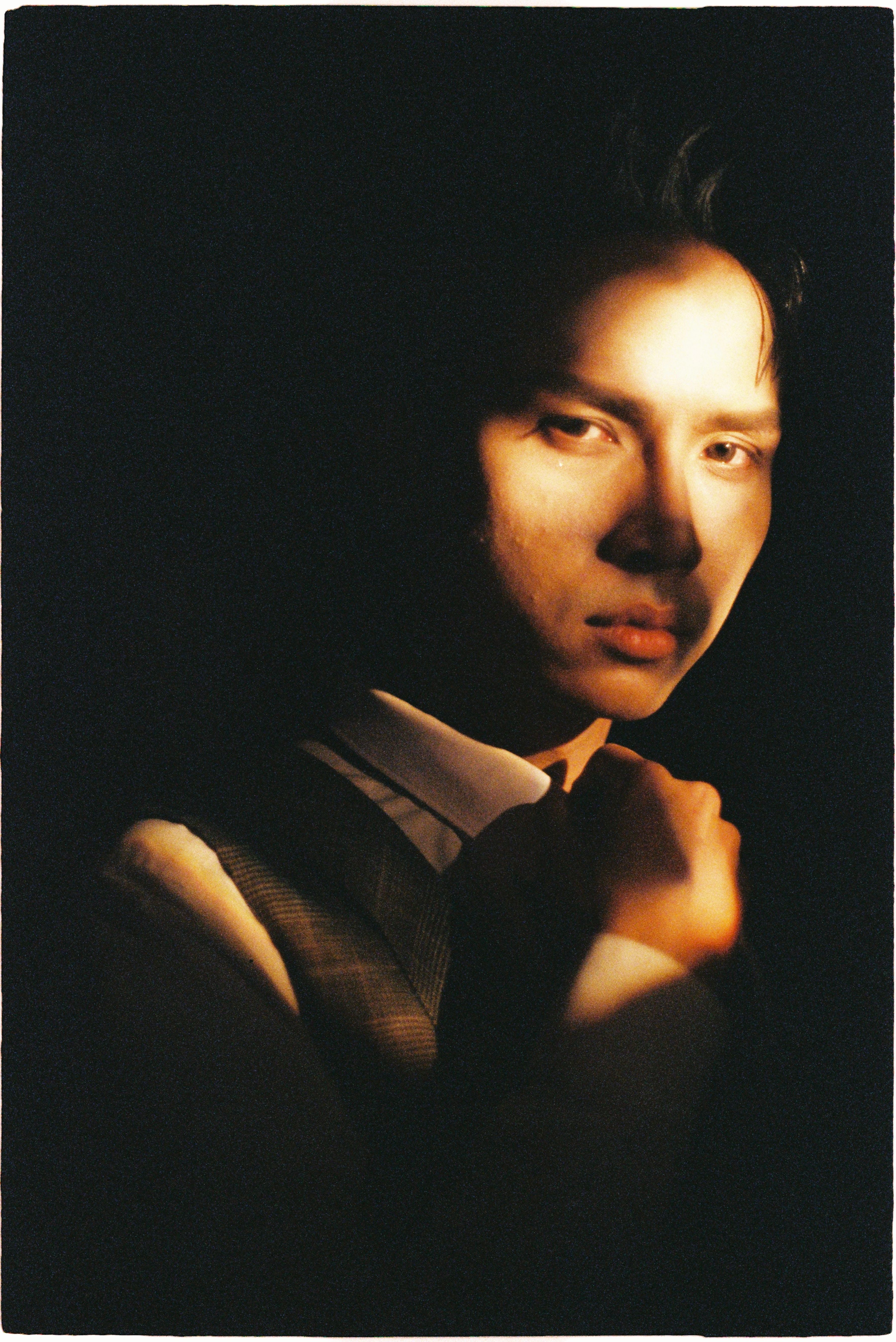 Moody portrait of a young adult in a dramatic lighting setting highlighting facial features.